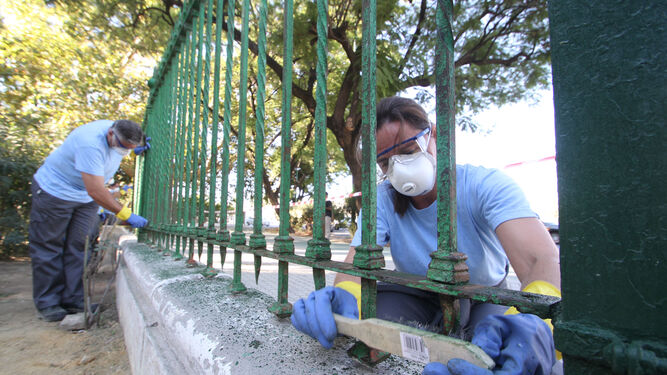 Dos de los 131 trabajadores contratados del sector agrícola lijan el enrejado junto a la Glorieta de los Marineros.