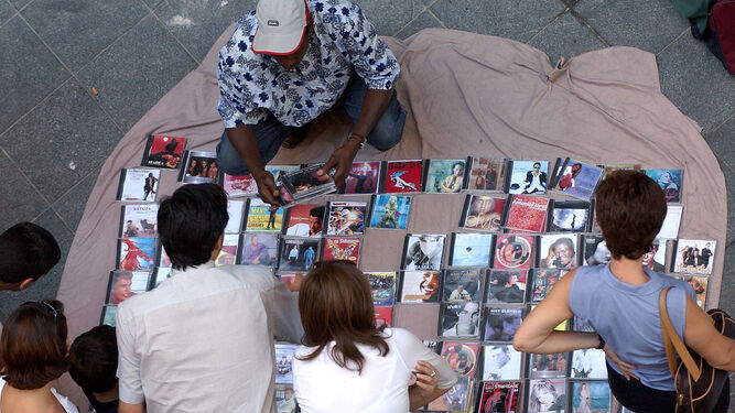 Un mantero ofrece copias de CDs a un grupo de personas en plena calle.