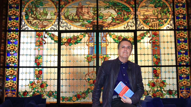 Juan Cobos Wilkins, con su último poemario en la mano, ante una de las imponentes vidrieras del Palacio Mora Claros.