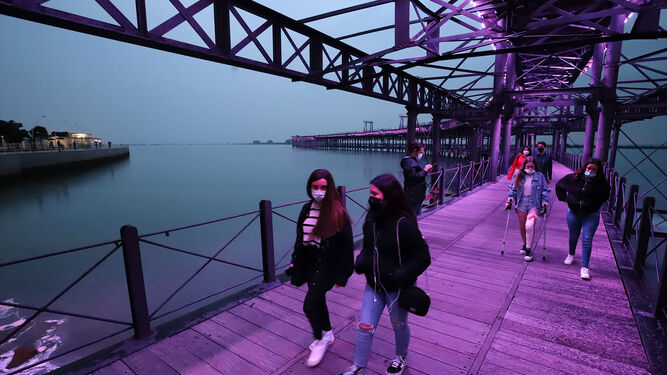 Mujeres caminando por el Muelle de la Riotinto, iluminado de morado por el 8M.