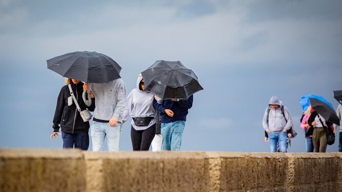 Varias personas pasean bajo la lluvia en Cádiz