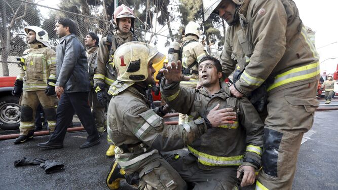 Dos bomberos atienden a un compañero ayer en el incendio de un centro comercial en Teherán.
