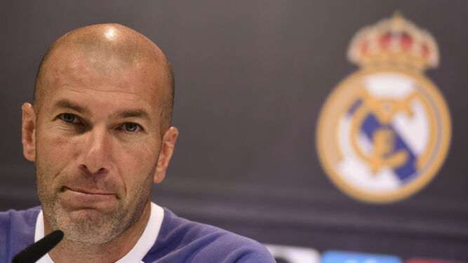 Zidane habla en la rueda de prensa con el escudo del Real Madrid de fondo.