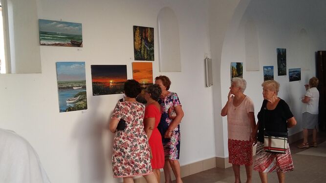 Un grupo de mujeres mira atentamente algunos de los cuadros de la exposición de Aramburu.