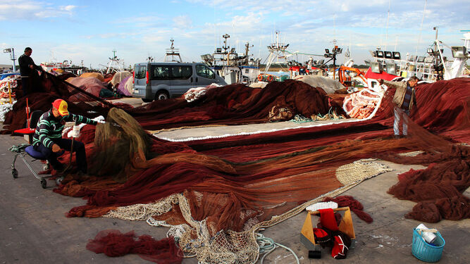 Unos rederos revisan y reparan las artes de pesca en el puerto de Punta Umbría.