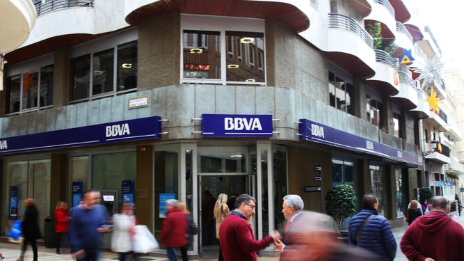 Dos personas dialogan frente a la oficina de BBVA en Huelva.