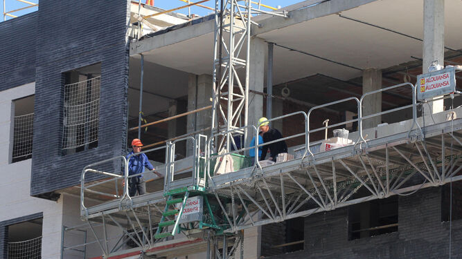 Tres obreros trabajan en la construcción  de un bloque.