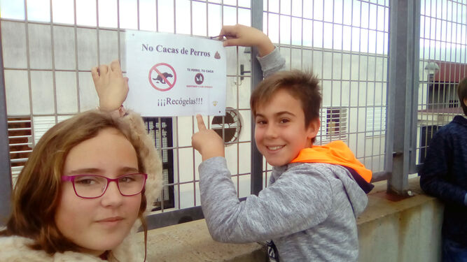 Dos escolares colocan uno de los carteles en una valla.