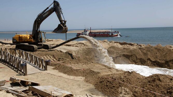 Una excavadora realiza trabajos de aportación de arena en la playa de El Portil.