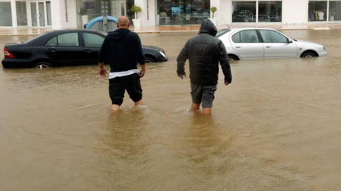 Dos hombres caminan con agua hasta las rodillas por una calle de Jávea (Alicante).