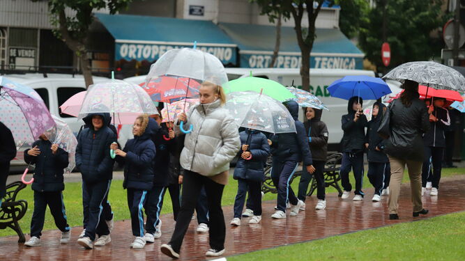 Pequeños estudiantes caminan de dos en dos con un paraguas para refugiarse de la lluvia.