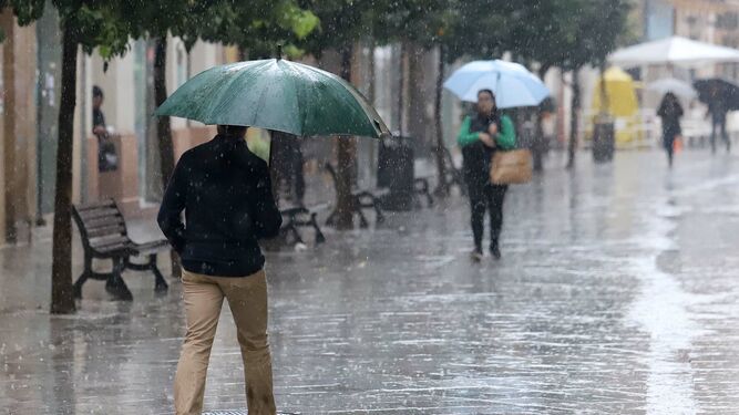 Onubenses transitan por una calle de Huelva en un día lluvioso.