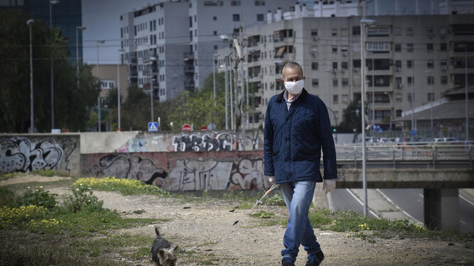 Un hombre pasea a su perro por un descampado de Sevilla ataviado con mascarilla y guantes.