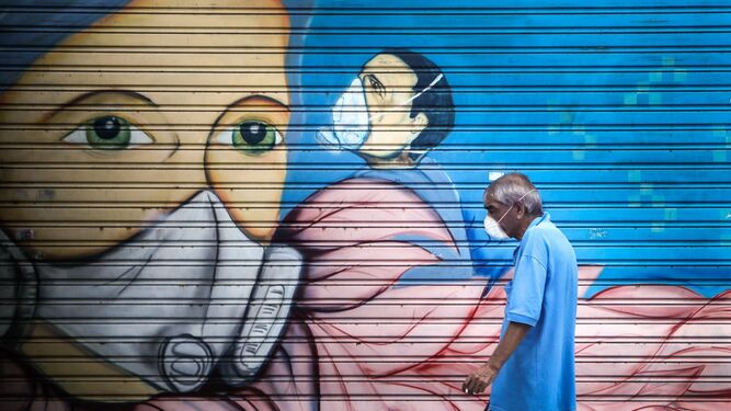 Un hombre con mascarilla pasa delante de un mural sobre el coronavirus