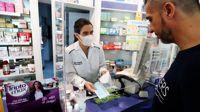Una farmacéutica muestra mascarillas a un cliente.