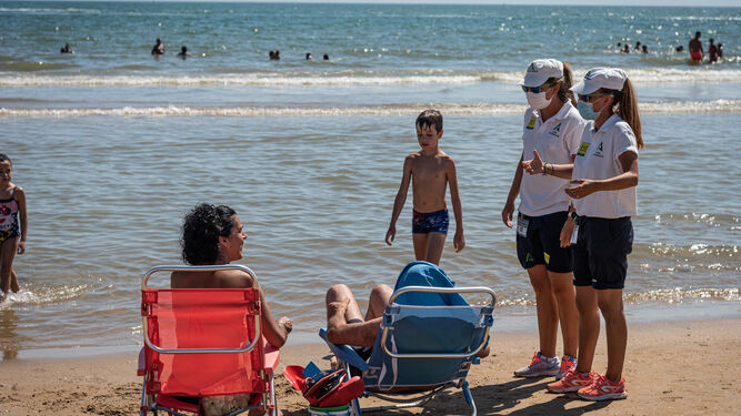 Unas auxiliares de playa informan a unos bañistas sobre el uso de la mascarilla.