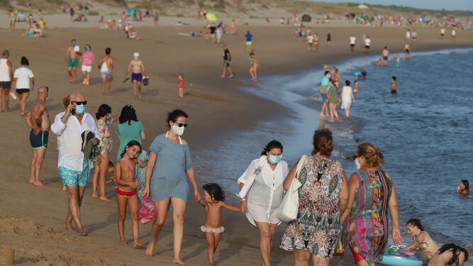 Varios grupos de personas pasean por una playa de la costa onubense al atardecer.