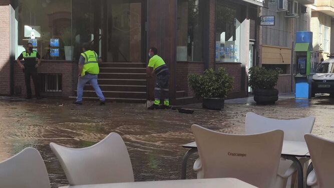 Un agente y varios operarios, trabajando en la zona para cortar la salida de agua en la calle Sor Ángela de la Cruz de Huelva.