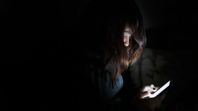 Una adolescente mira el móvil en la oscuridad.