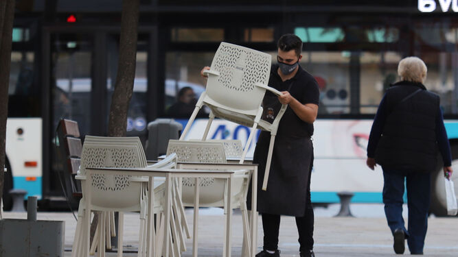 Un camarero recoge las sillas y mesas de una terraza en Huelva.