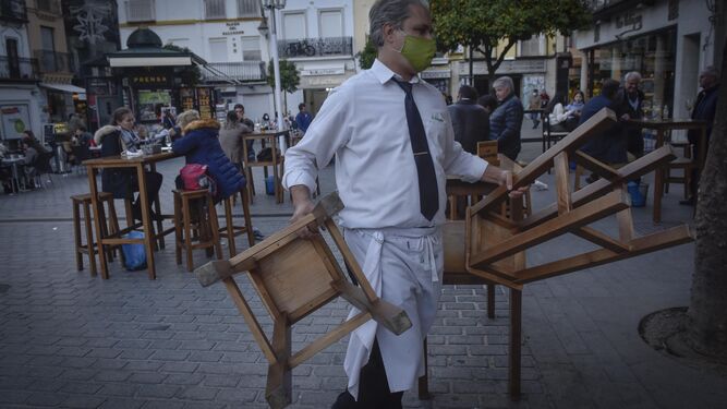 Un camarero recogiendo los taburetes de la terraza de un bar de la Plaza de El Salvador.