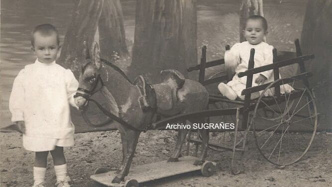 Unos niños en un carrito con su caballo de cartón.