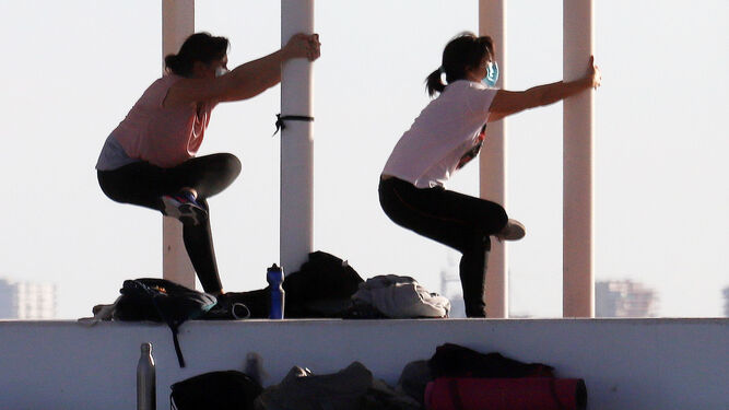 Dos mujeres realizan ejercicios de estiramiento en el entorno del Paseo de la Ría.