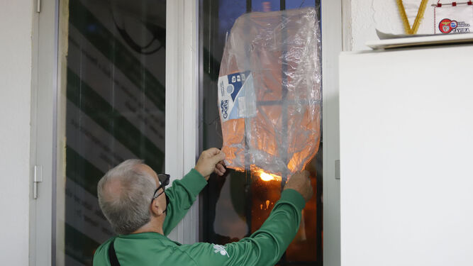 El presidente de la asociación vecinal cubre con un plástico la rotura en una ventana.