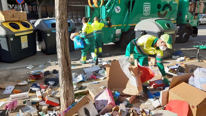 Operarios de los servicios de limpieza retirando los restos de los regalos de Reyes depositados junto a los contenedores.