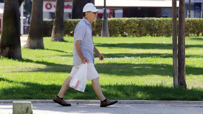 Un hombre pasea con su gorra para protegerse del sol.