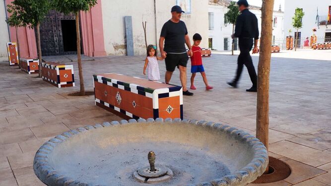 Una familia pasa junto a una fuente de beber seca en la plaza de Higuera de la Sierra.