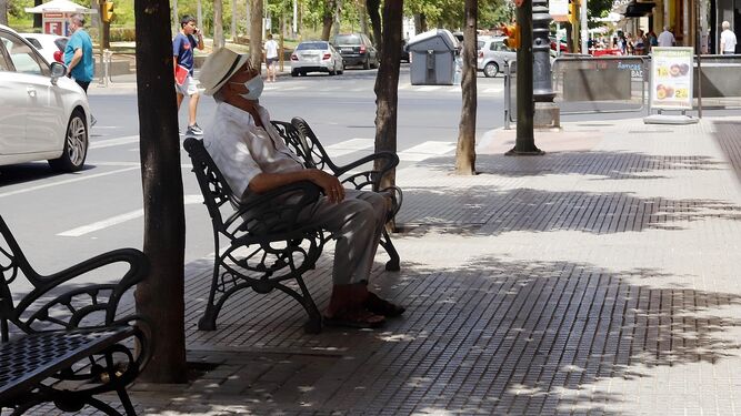 Una persona descansa del calor en un banco a la sombra.