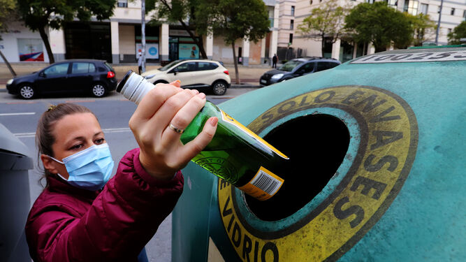 Una joven echa una botella al contenedor verde.