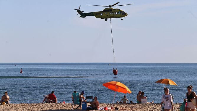 Un helicóptero del Infoca recoge agua en la playa de El Portil en presencia de bañistas este miércoles pasado.