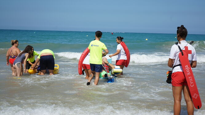 Varias personas dependientes se bañan en la playa de Camposoto con la ayuda del personal.