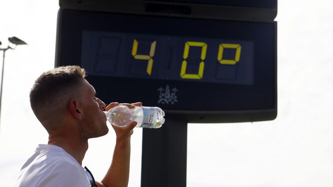 Un joven bebe agua junto a un termómetro.