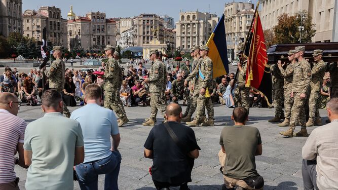 Varias personas se arrodillan al paso del féretro de un militar en Kiev.