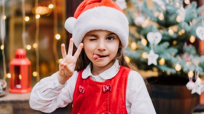 Una niña marca el número tres con sus dedos y con un gorro de Papá Noel.