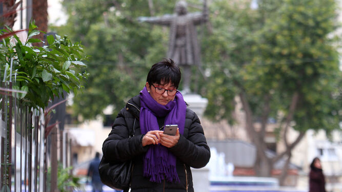 Una mujer camina abrigada por las calles de Huelva mientras utiliza su teléfono móvil