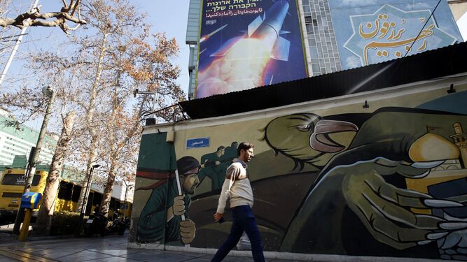 Un hombre pasea en una calle de Teherán junto a un cartel con un cohete que reza "Preparad vuestros ataudes"