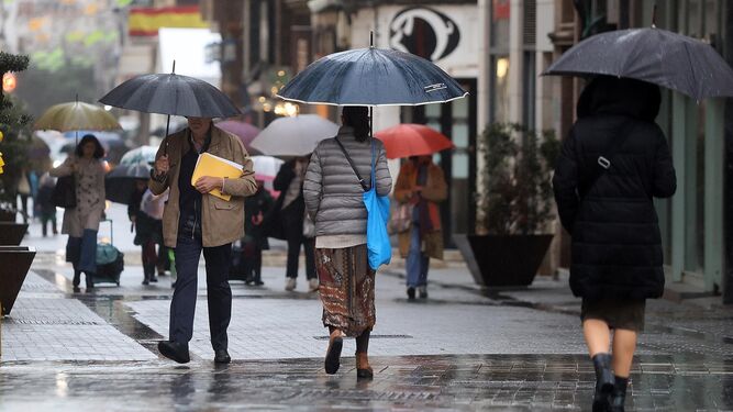 Onubenses pasean por el centro de la capital con sus paraguas.