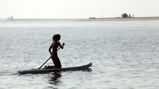 Una joven practica pádel surf en una playa de la costa onubense