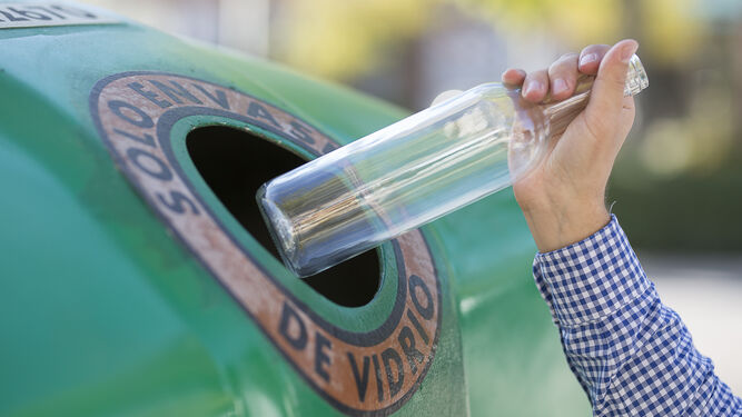 Un hombre introduce una botella de vidrio en el contenedor verde.